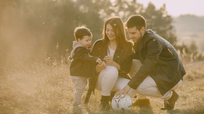 A cheerful family bonding outdoors with a soccer ball, enjoying a sunny day in the grass.
